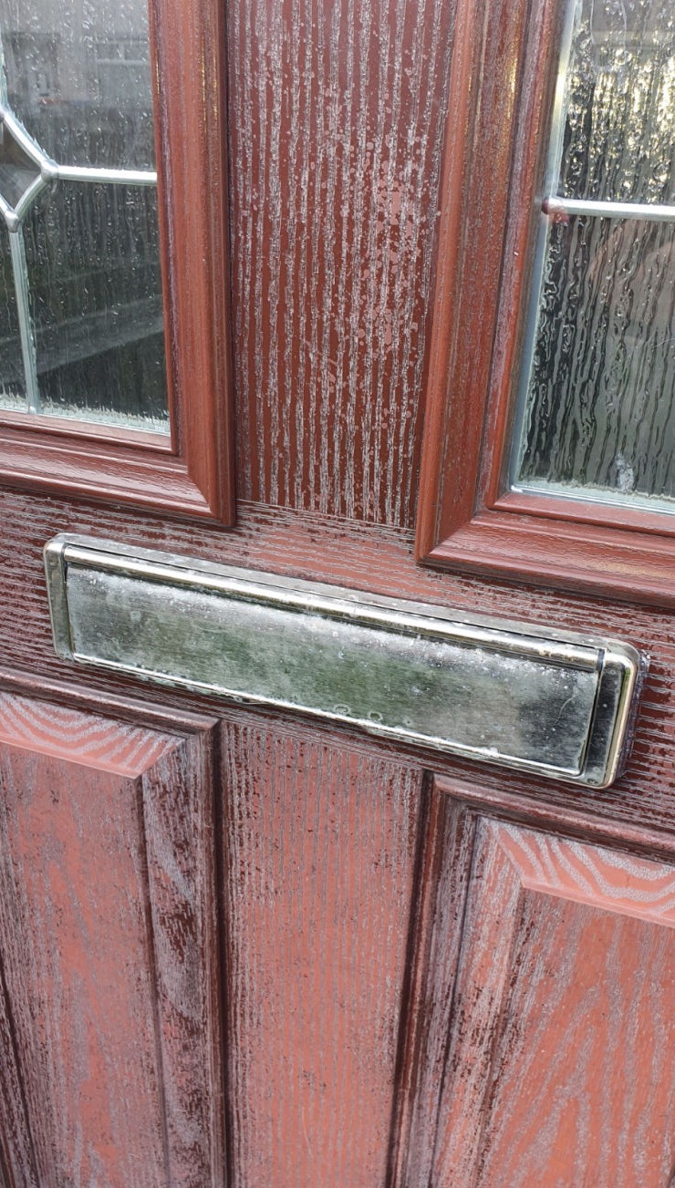 image shows the centre section of a faded composite door with gold letterbox 