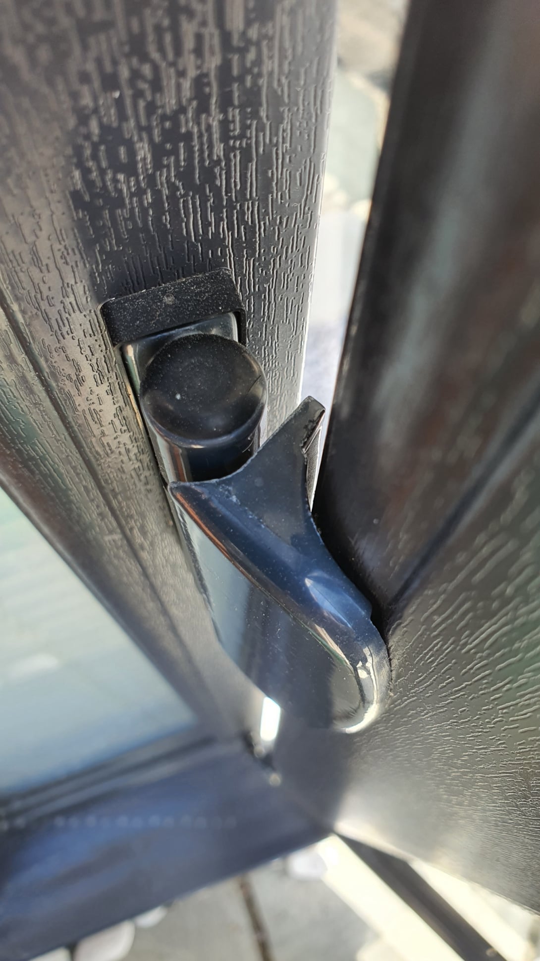 “Close‑up of a uPVC door hinge mechanism during repair, showing the metal friction stay, screws and corner buffer with tools visible in the background.