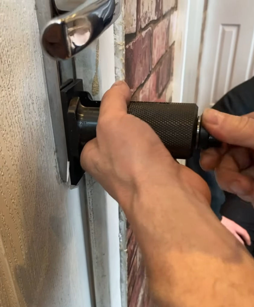 The image shows someone using a professional tool, probably a door spreader, to safely open a door. The door has the number 